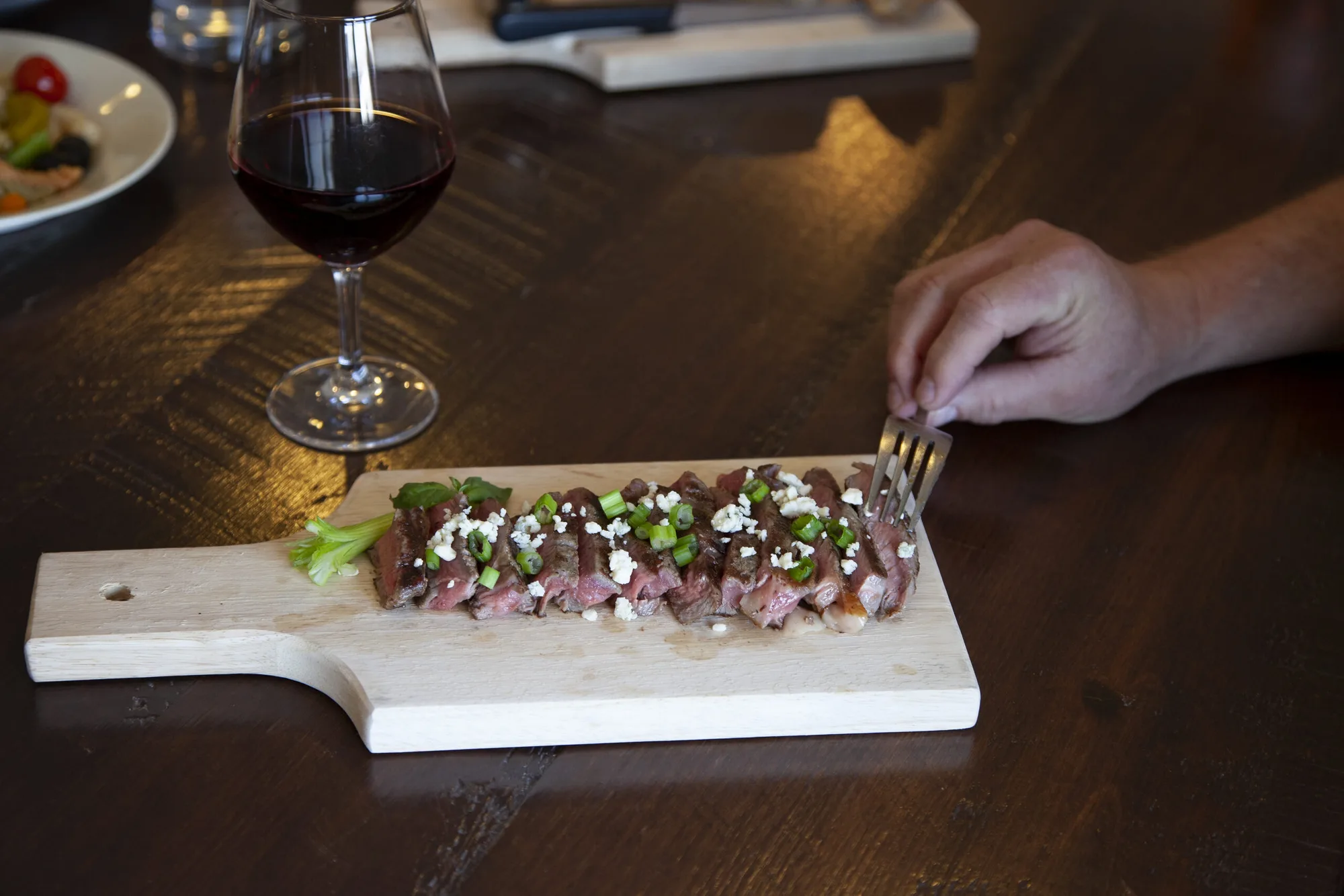 Guest enjoying sliced steak with red wine at a rustic Lazy J lodge dining table